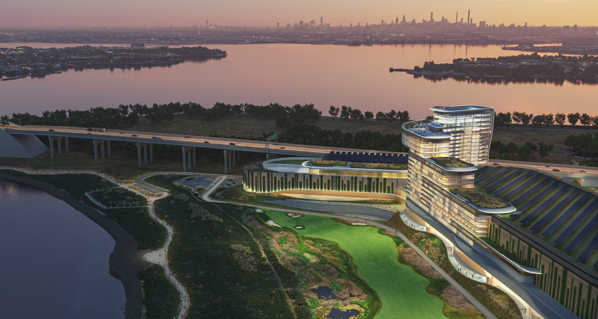 Modern waterfront building with curved architecture, surrounded by greenery and water, at dusk with a city skyline in the background.