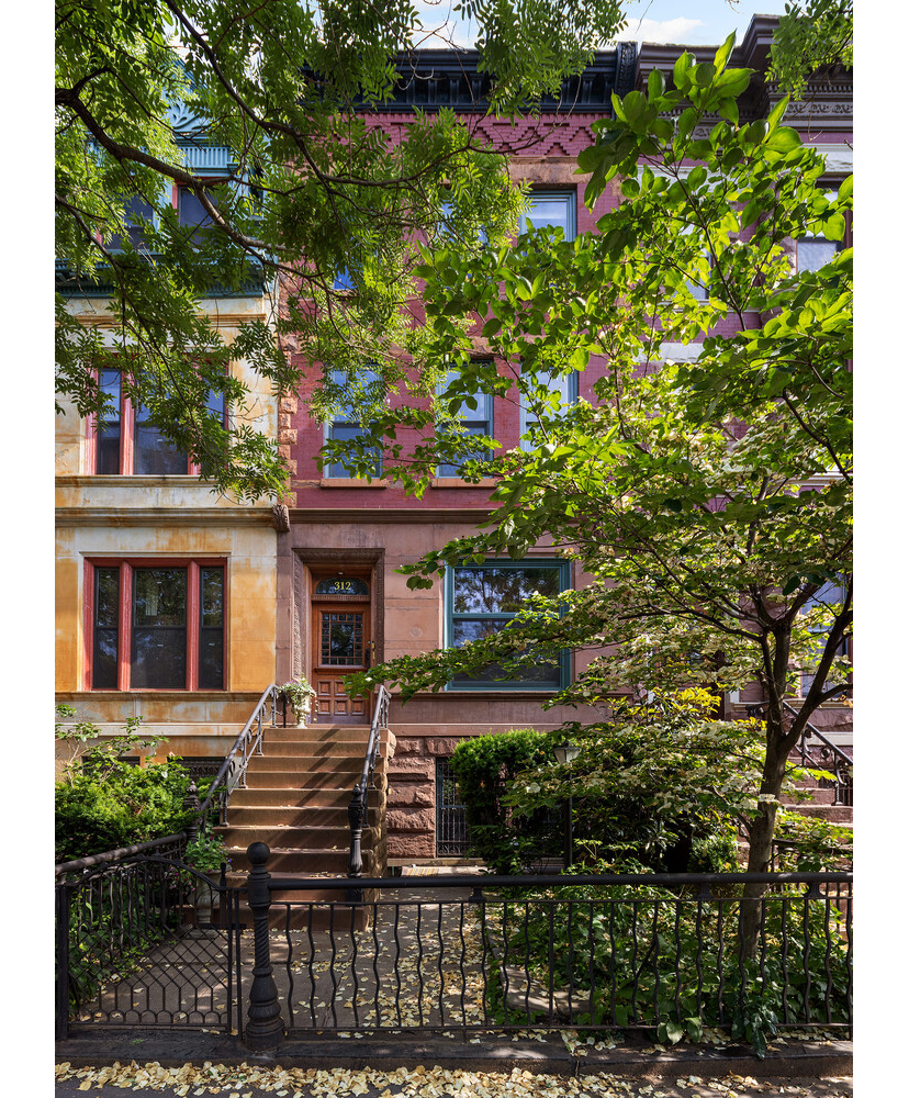 brick and brownstone exterior of a row house mostly covered by trees
