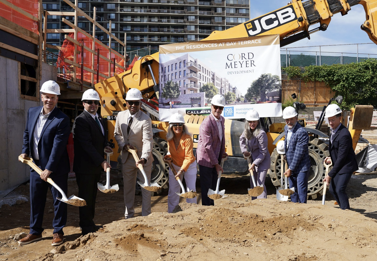 Eight people in hard hats hold shovels during a groundbreaking ceremony in front of construction machinery and a banner for Cord Meyer Development.