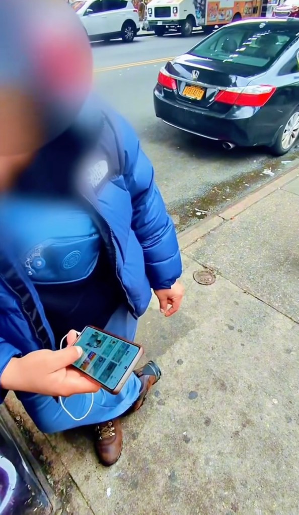 A person in a blue jacket holds a phone on a city street.