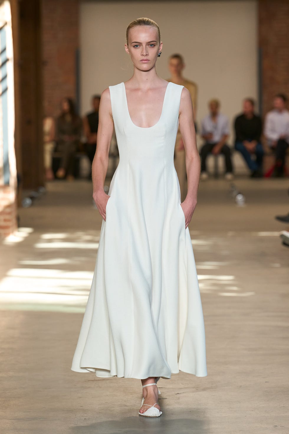 A model walks the runway wearing a sleek, white dress with a deep neckline and minimalistic design.