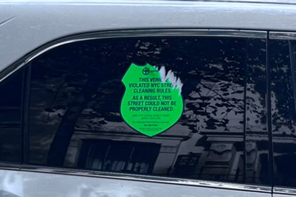 A bright green sticker on a car window reads, "THIS VEHICLE VIOLATED NYC STREET CLEANING RULES. AS A RESULT, THIS STREET COULD NOT BE PROPERLY CLEANED."