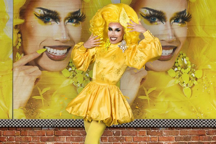 Tequila Thirst wearing a yellow dress with a large yellow wig she is holding onto.