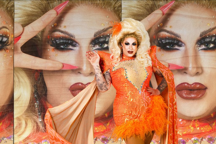 Ky Kelly wearing an orange dress, smiling ahead with one hand in the air.