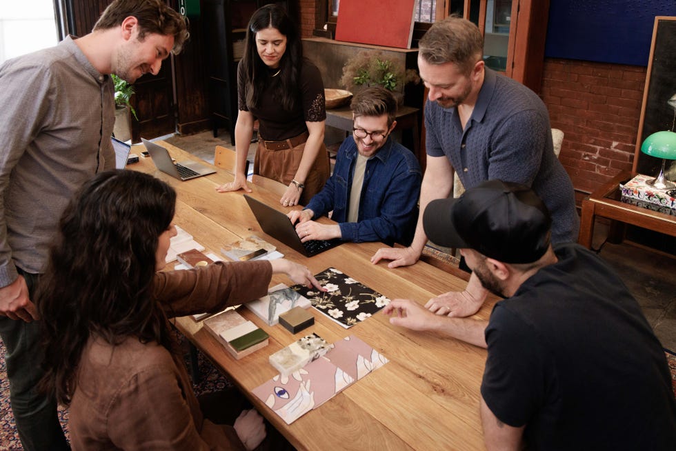 A group of people collaborating around a table with materials and a laptop in a creative workspace.