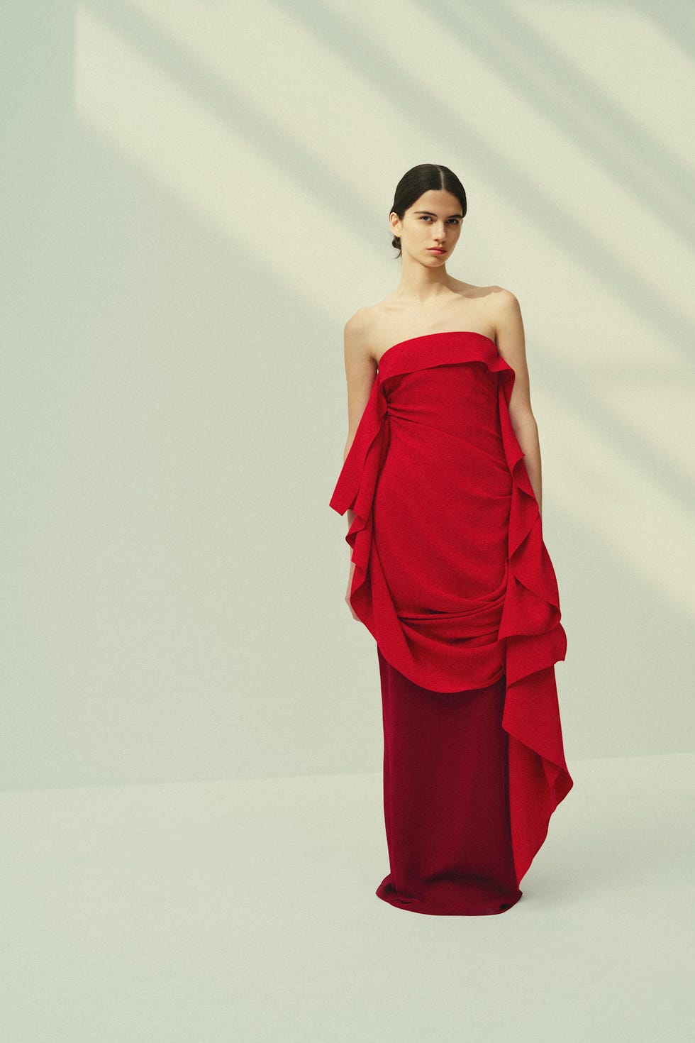 Elegant model in a bold red strapless gown with draped fabric against a minimalist background.