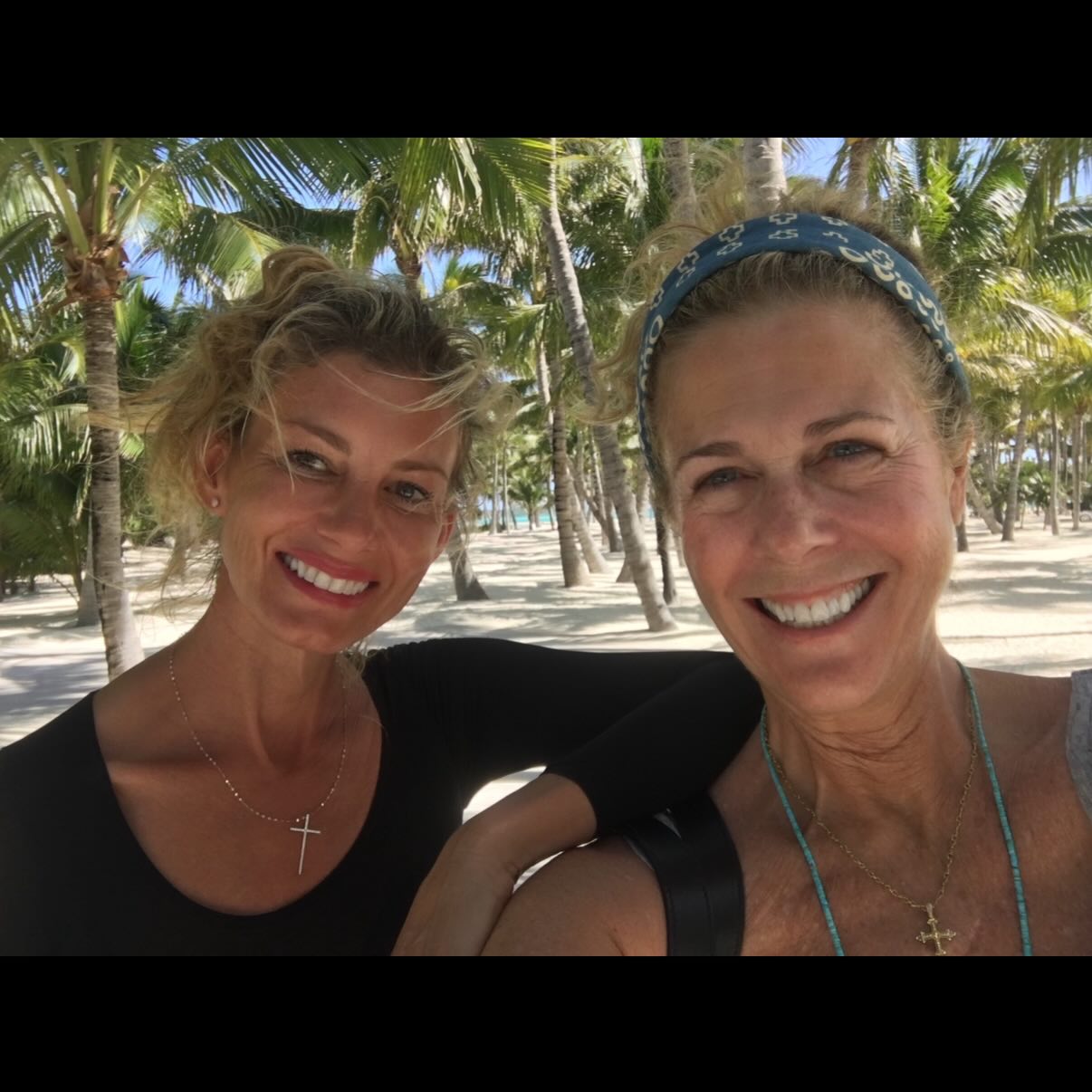 Faith Hill and Rita Wilson smiling in front of palm trees on a beach.