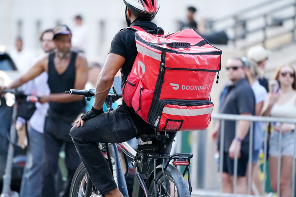 A person riding an e-bike in New York with a red DoorDash delivery bag on their back.