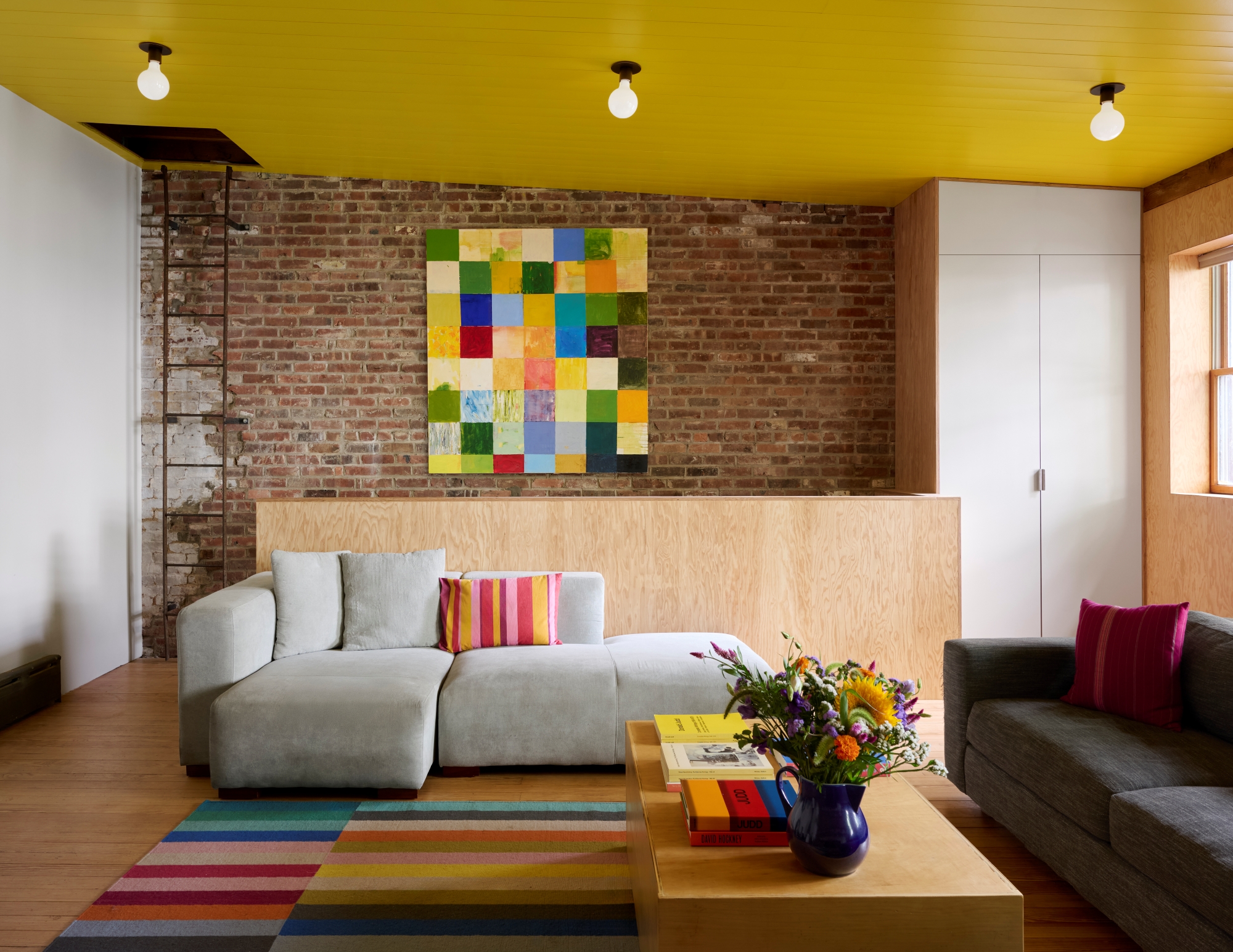 ROOM WITH YELLOW CEILING BRICK WALL, COLORFUL ART AND RUG
