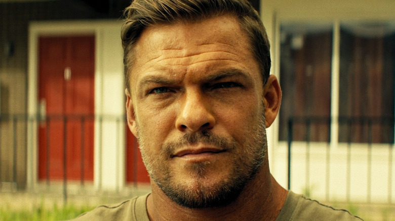 Alan Ritchson as Jack Reacher standing outside in a residential area