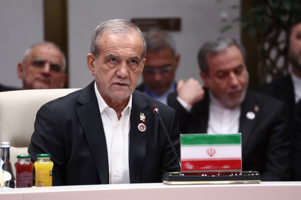 Iranian President Masoud Pezeshkian speaking at the SCO summit, with an Iranian flag in front of him.