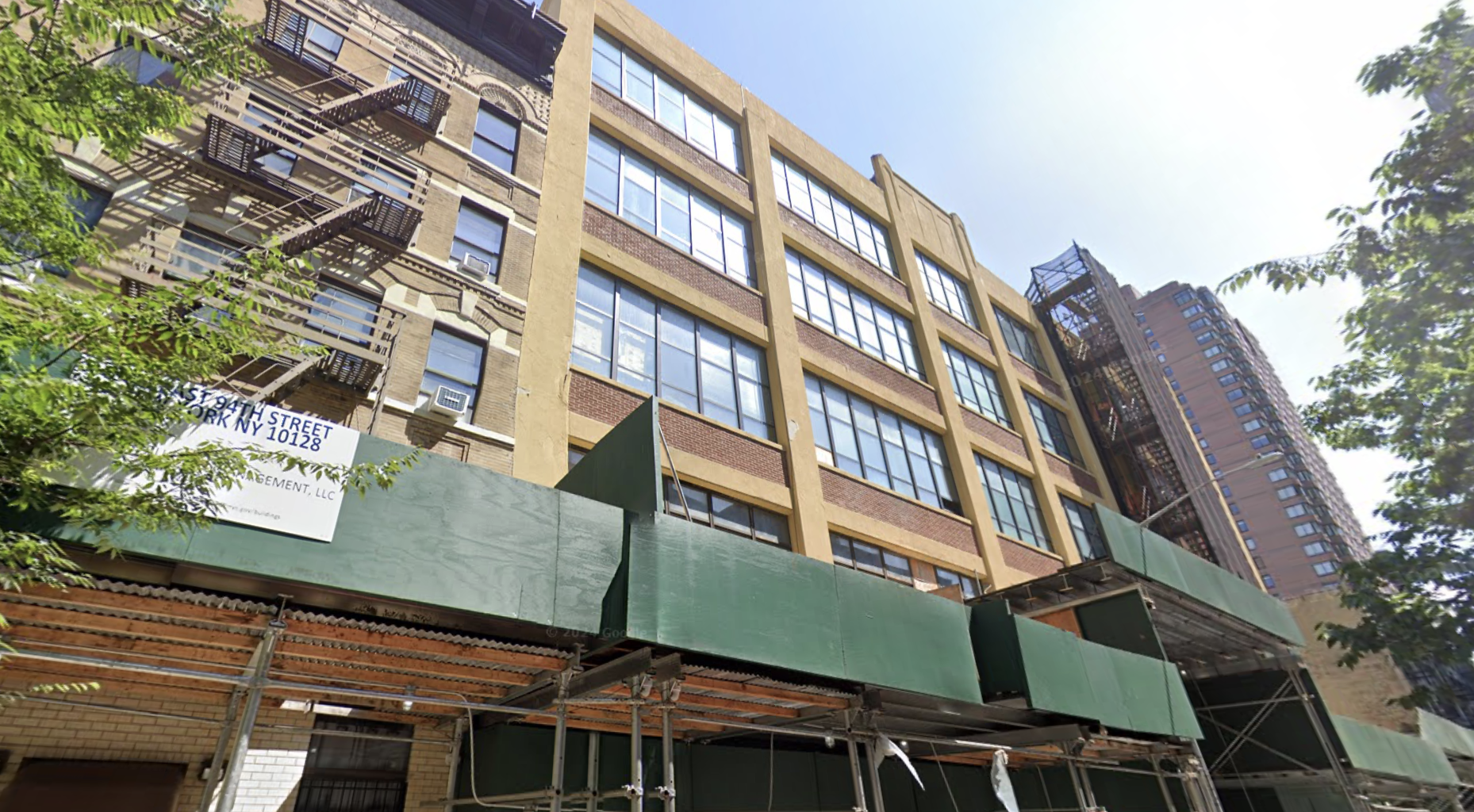 Street view of a mid-rise building with fire escapes and green construction scaffolding in an urban area, under a clear sky.