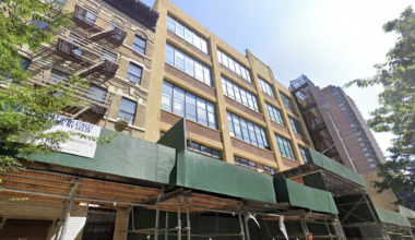 Street view of a mid-rise building with fire escapes and green construction scaffolding in an urban area, under a clear sky.