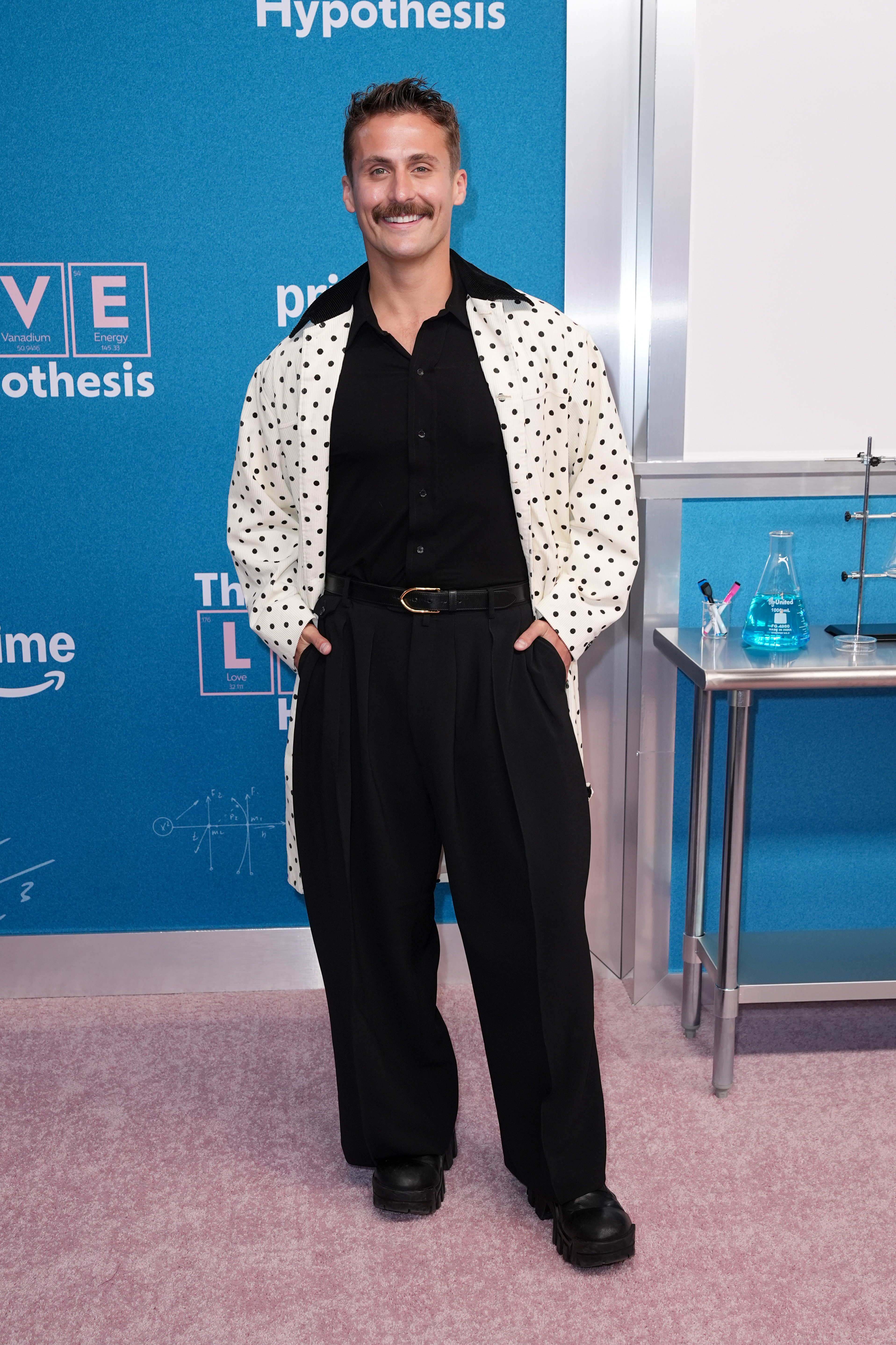 Julian Burzynski at "The Love Hypothesis" New York Premiere, wearing a black shirt, black pants, and a white polka-dotted jacket.