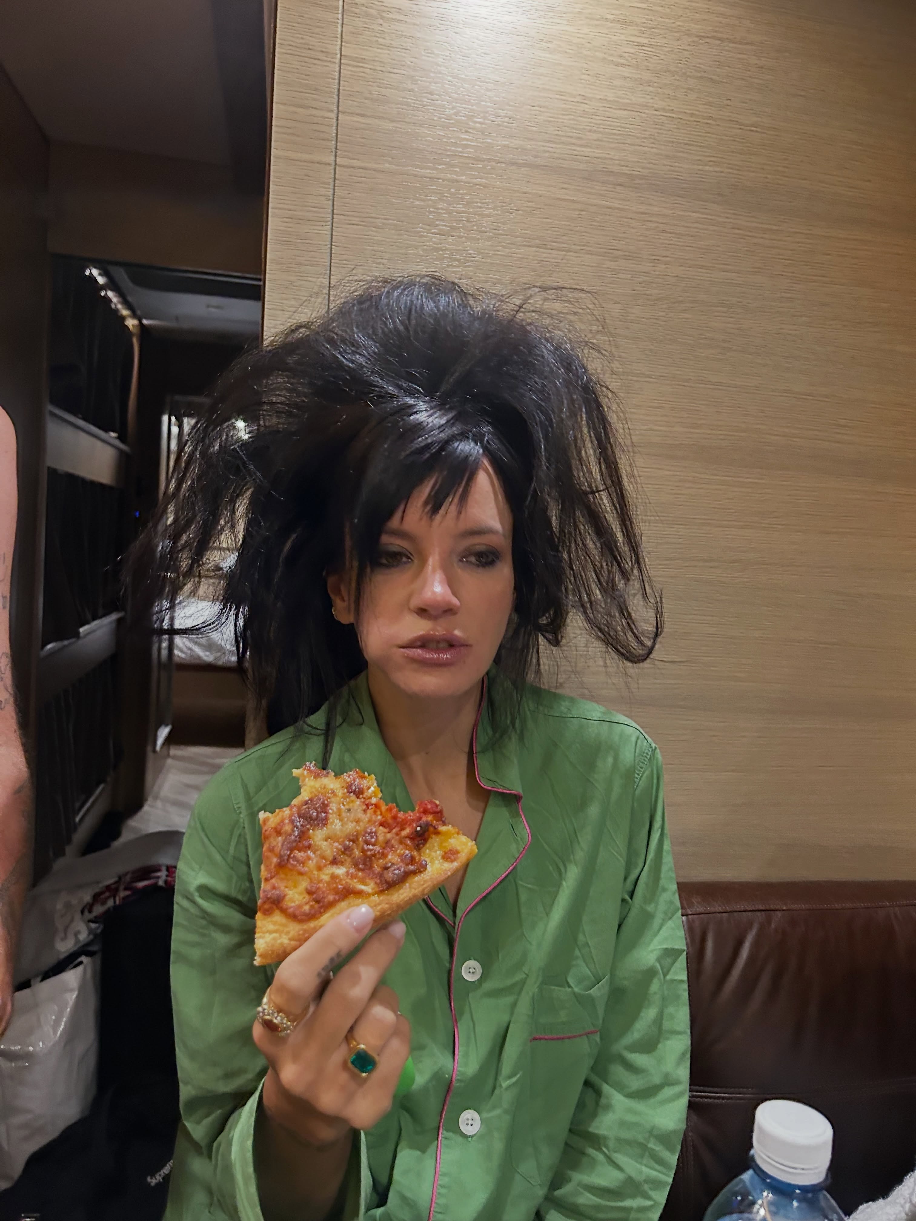Lily Allen wearing green pajamas, holding a slice of pizza.