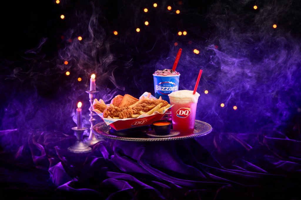Dairy Queen's Halloween lineup: a chicken strip basket, a red drink with foam, and a Blizzard, all on a silver tray with candles and purple mist.