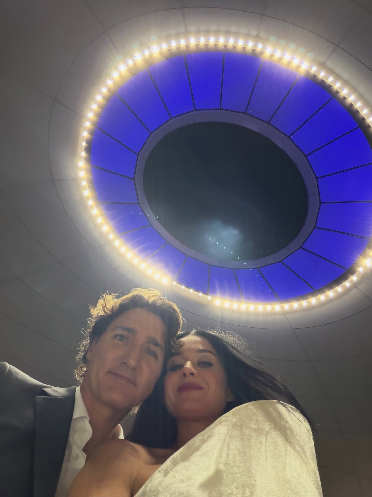 Katy Perry and Justin Trudeau posing together under a circular, illuminated ceiling.