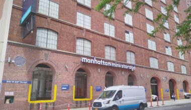 Brick building with large windows labeled "Manhattan Mini Storage." A white van is parked in front, and a person walks on the sidewalk.