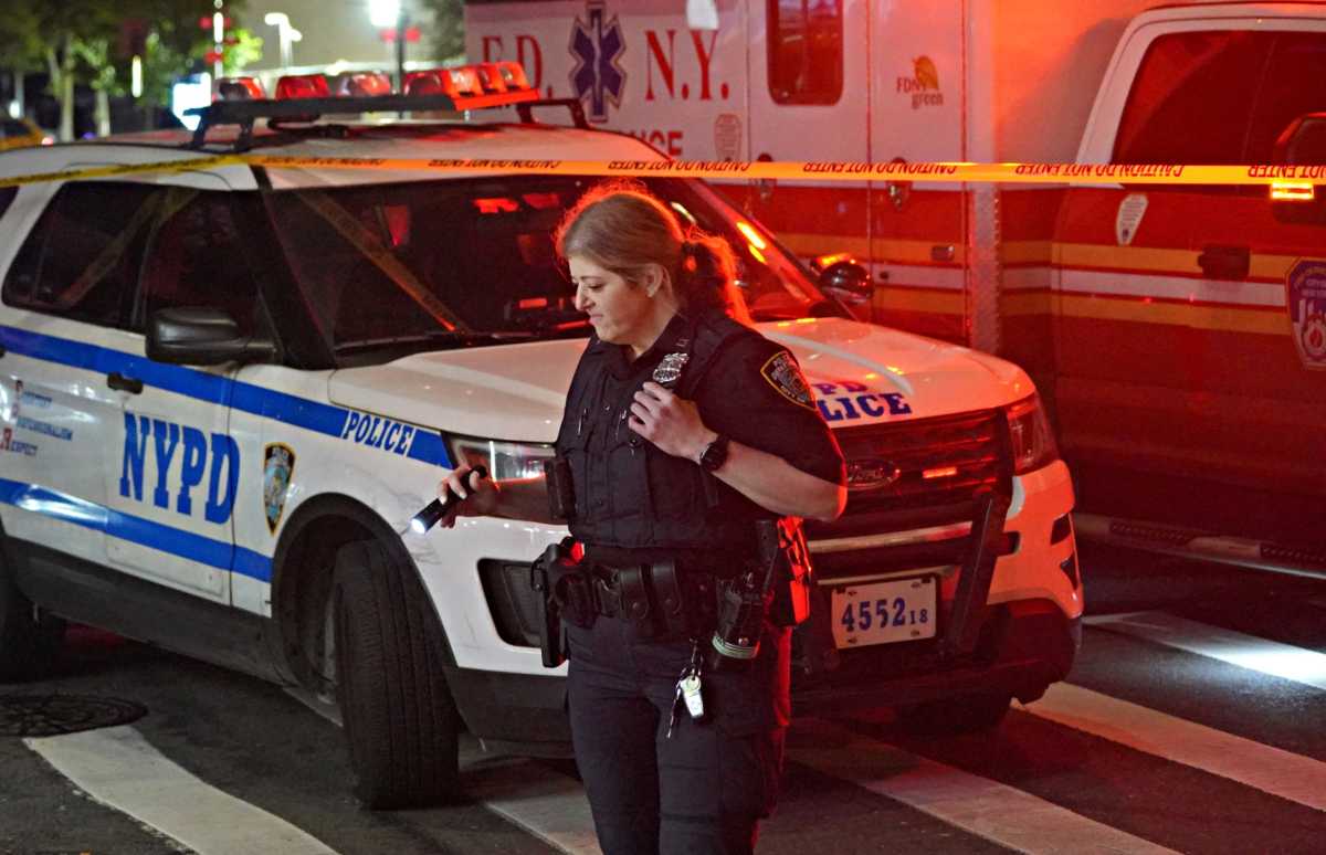 Police officer in front of NYPD car and EMS vehicle at scene of crime in Queens