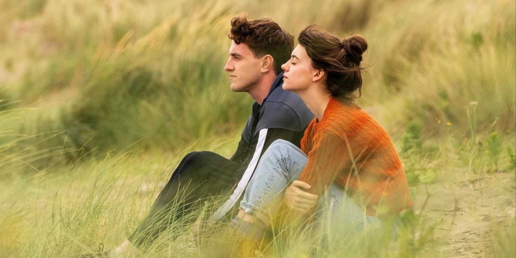 Daisy Edgar Jones and Paul Mescal sitting on a field in Normal People.