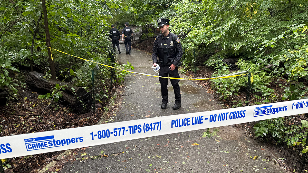 NYPD officers stand behind police tape on a wooded Central Park path