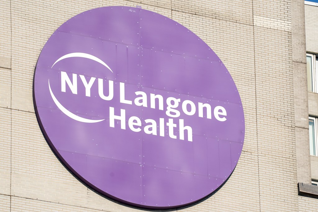 The NYU Langone Health logo, a purple circle with "NYU Langone Health" in white text, attached to a brick building.