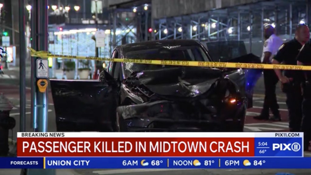A black Tesla with significant front-end damage, marked off by yellow police tape, at the scene of a fatal crash in Midtown Manhattan.