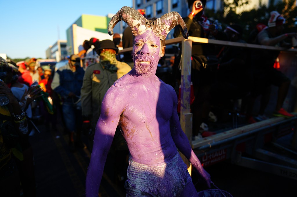 A man with purple body paint and horns on his head smiles during J'Ouvert celebrations in Brooklyn.