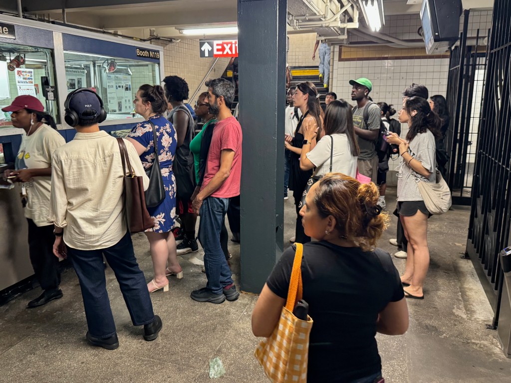 Crowd of people gathered at the Booth N119 ticket booth inside the Kingston-Throop Aves subway station.
