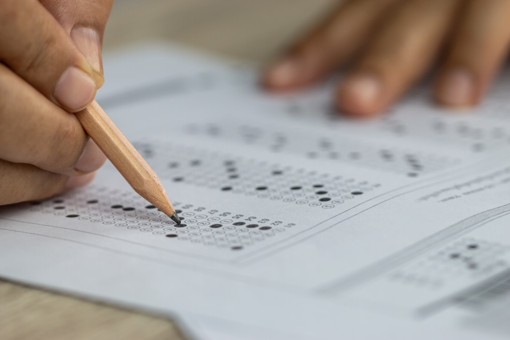 A student's hand holding a pencil and filling in bubbles on a standardized test answer sheet.
