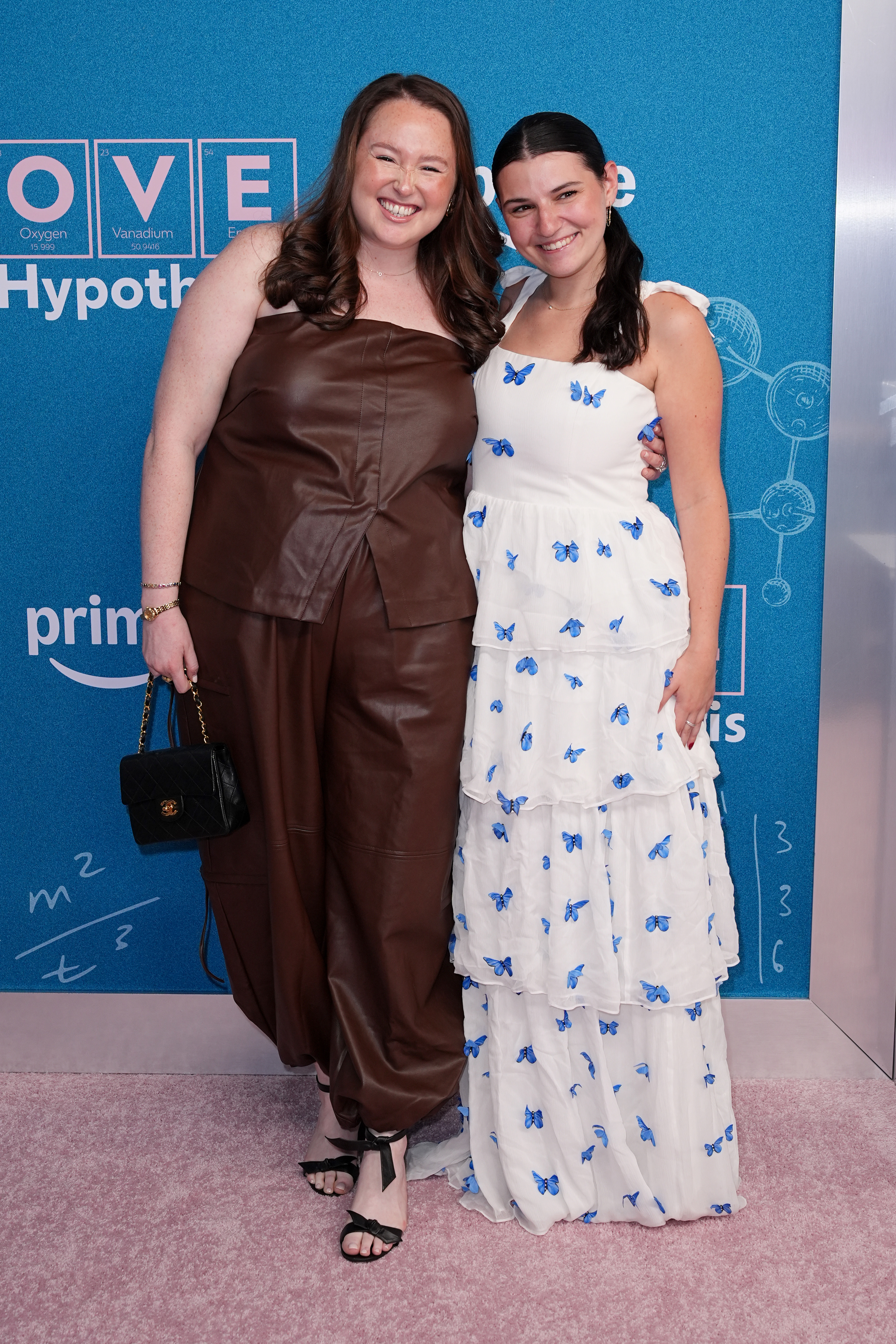 Sophie Beren in a brown leather outfit and Carly Heitner in a white dress with blue butterflies pose at "The Love Hypothesis" New York Premiere.