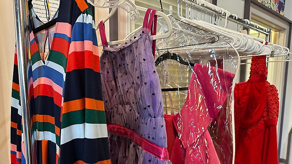A clothing rack with four bright pieces of clothing hanging from it is seen.