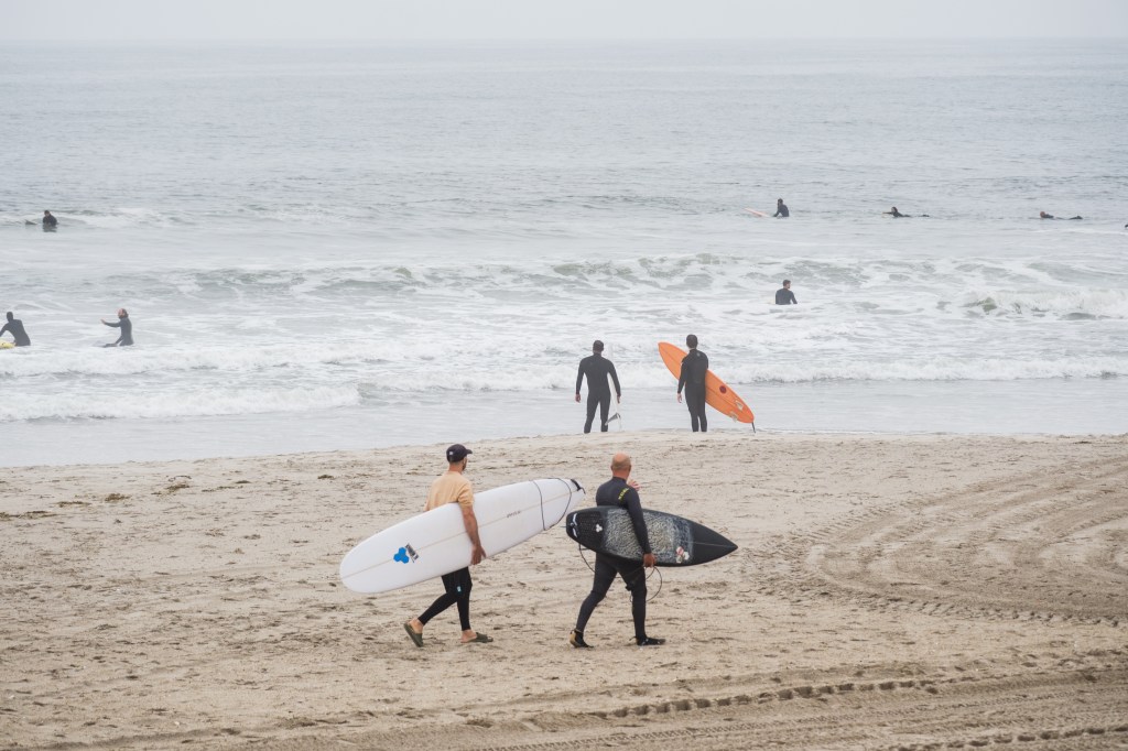 Several surfers in wetsuits with their boards on an overcast day at Rockaway Beach.