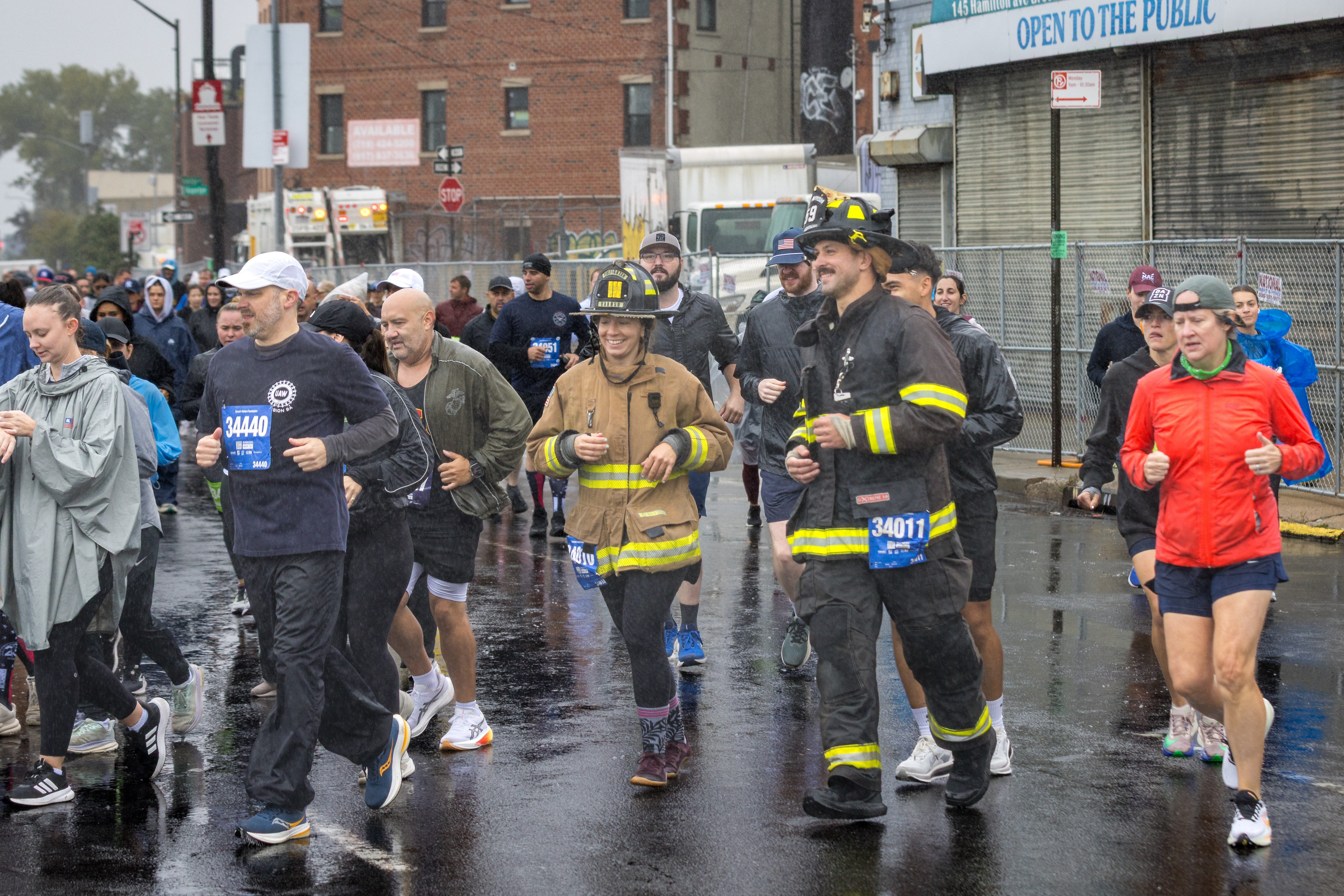 Participants, including firefighters, running in the annual Tunnel to Towers 5K Run & Walk NYC on a wet street.