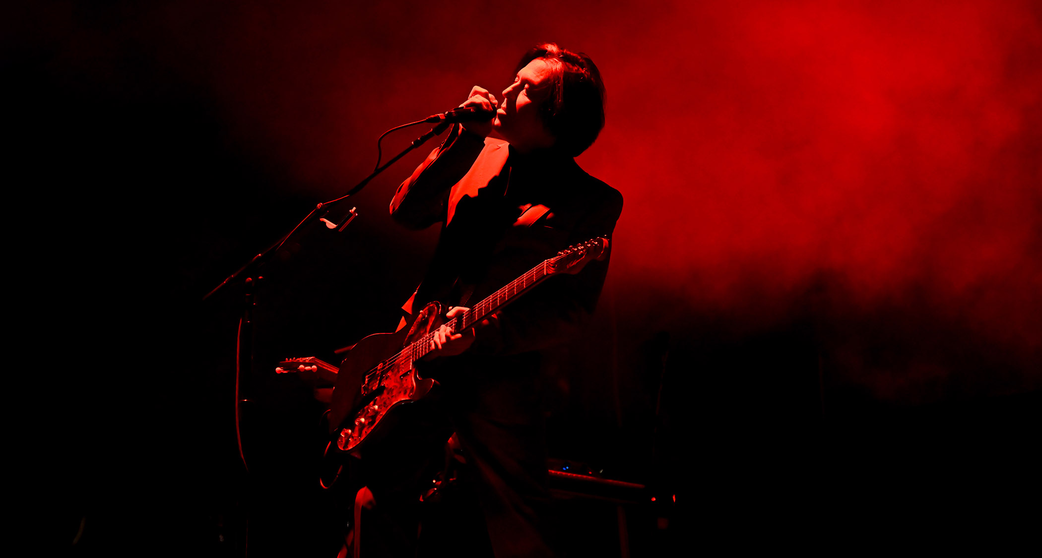 Troy Van Leeuwen is bathed in red stage lights