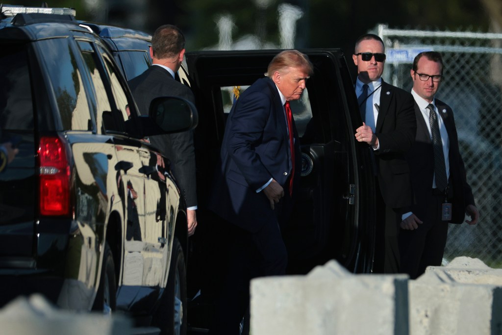 Donald Trump steps out of his motorcade accompanied by security personnel.