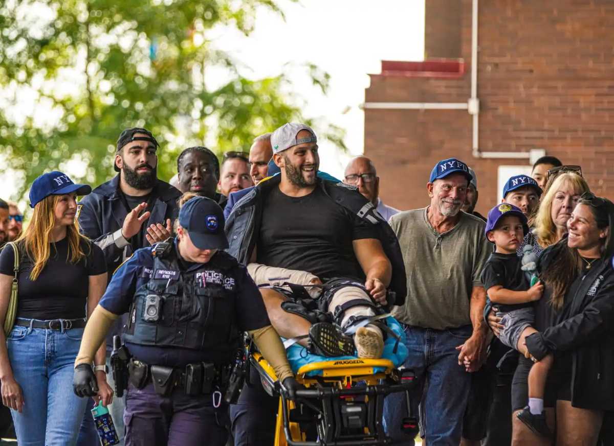 Det. Fisher smiled as he was wheeled on a stretcher out of Jamaica Hospital Medical Center on Aug. 25, 2025 with his family walking alongside him.