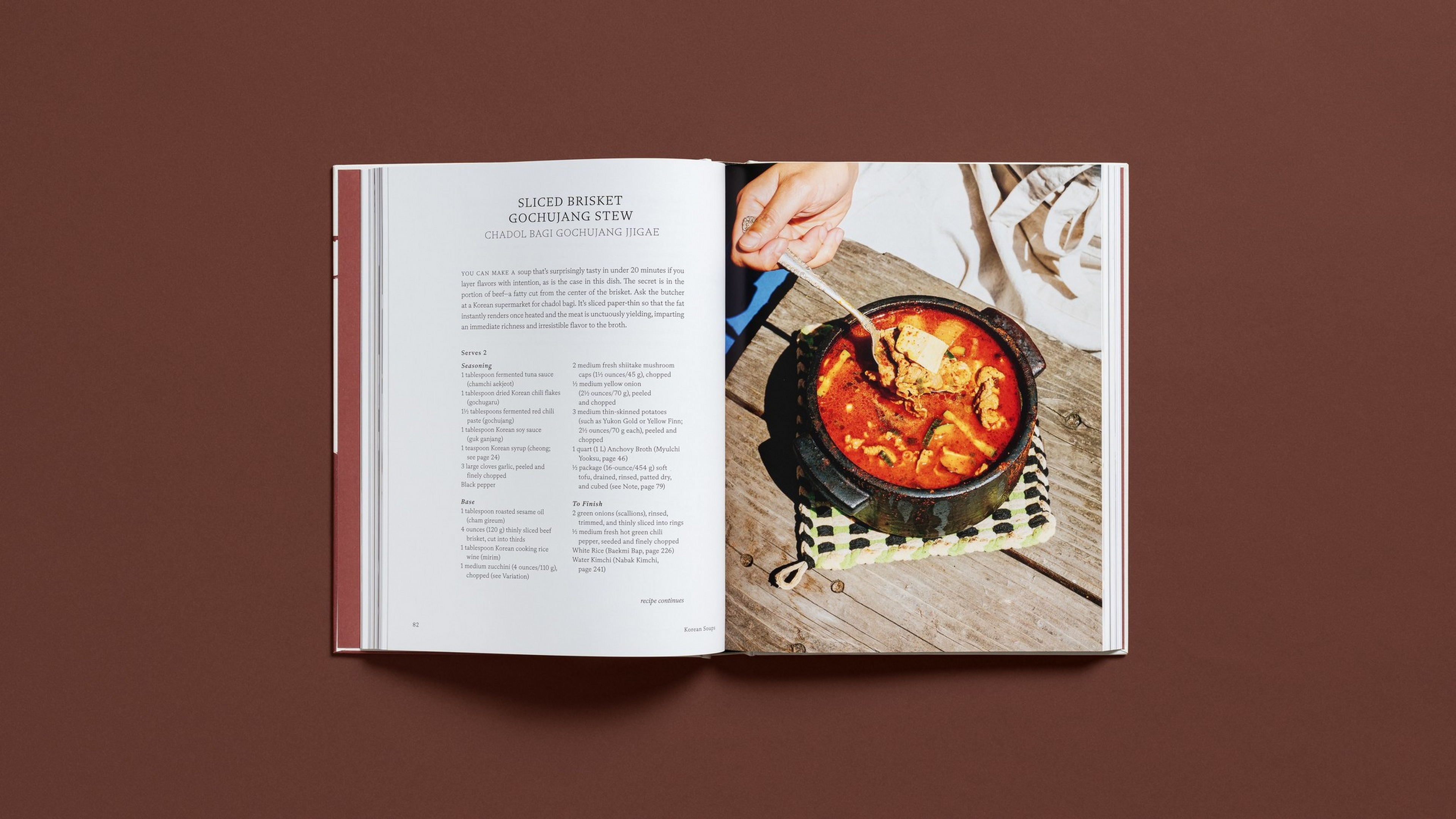 A cookbook open to a recipe for sliced brisket gochujang stew, with a photo of the stew in a black pot and a hand stirring it with chopsticks.