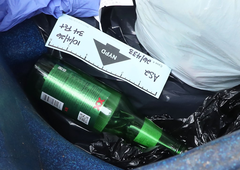 An NYPD evidence tag rests on a green glass bottle inside a garbage can.