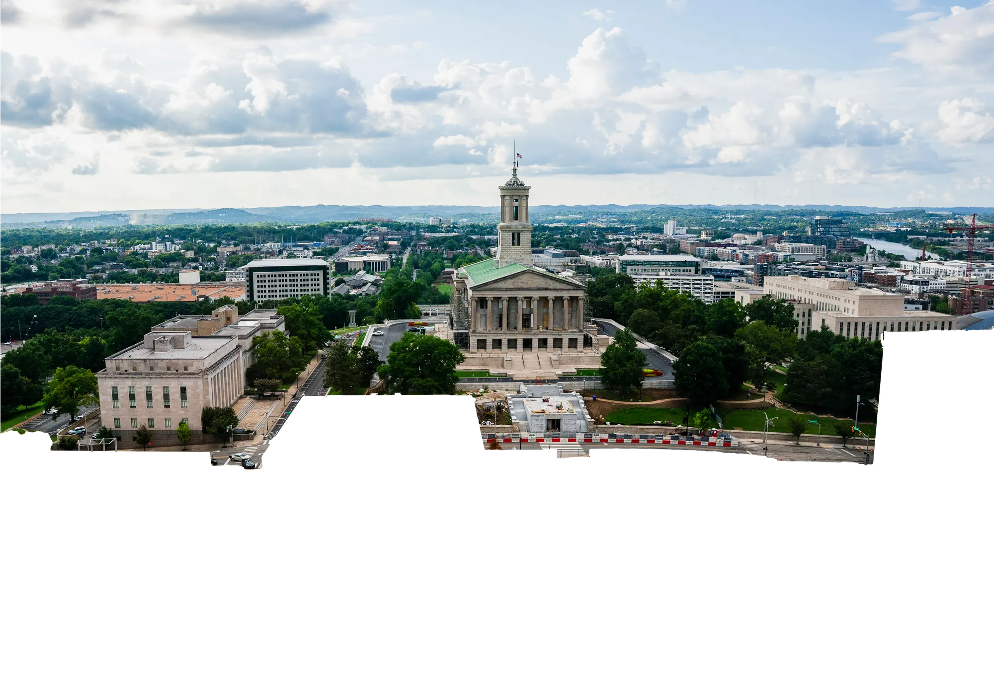 An aerial view of the Tennessee State Capitol in Nashville, the domed building on its hill above the city, with downtown and construction sites spreading out below it.