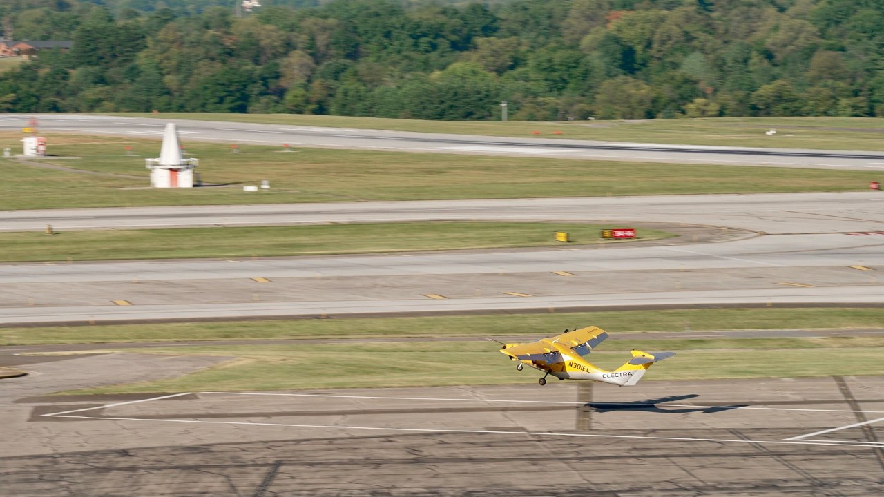 The yellow Electra EL2 hybrid-electric demonstrator lifting off from a small marked landing area at Roanoke-Blacksburg Regional Airport