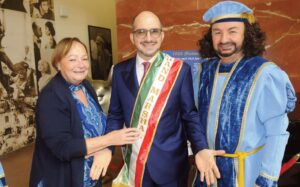 Parade Grand Marshal Giuseppe Commisso, the CEO of Mediacom Communications, gets his sash pinned by FIAOQ Executive Director Angie Markham as Christopher Columbus (aka Joe DiRico) enjoys the ceremony. Photos by Walter Karling