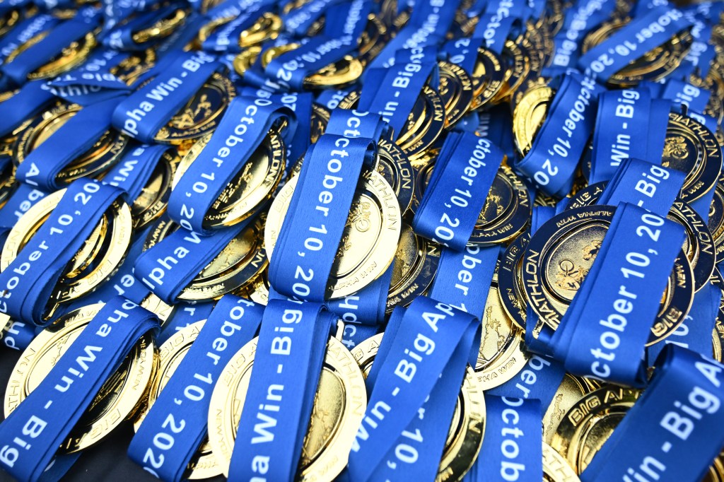 A pile of gold finisher medals with blue ribbons from the Big Apple Triathlon.