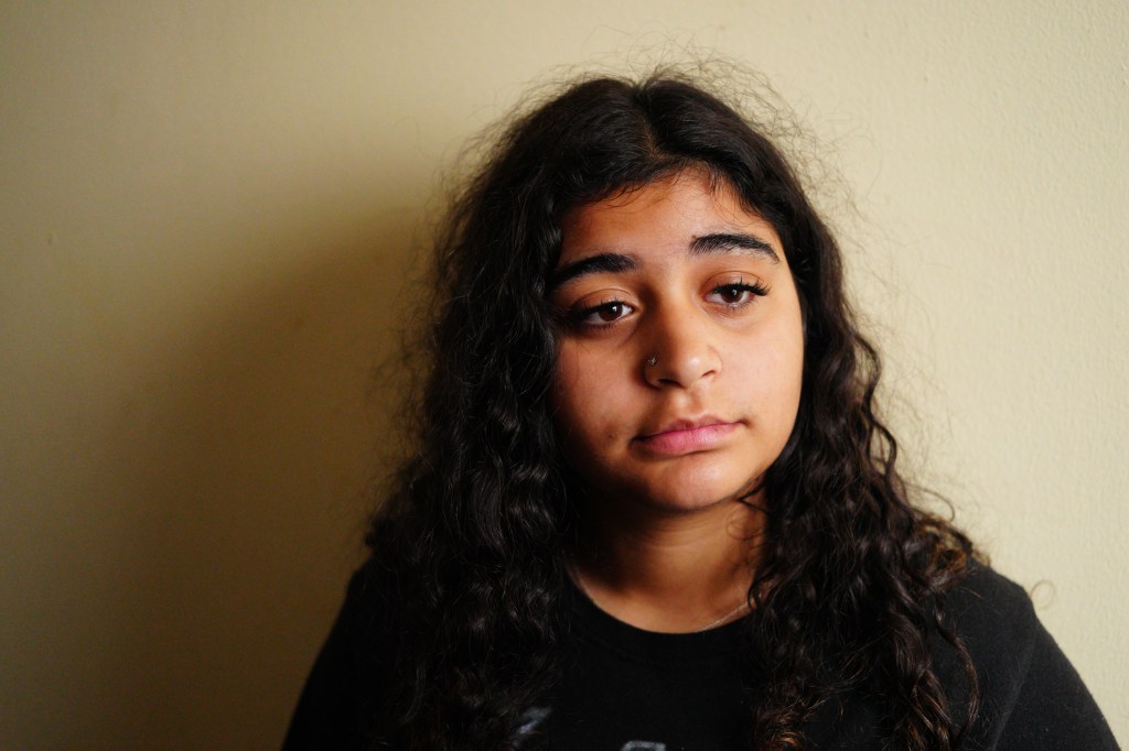 Miral Alamouri looking down with a somber expression against a neutral wall.