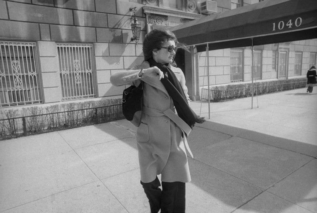 A recently widowed Jacqueline Onassis turns her head and raises her arm to avoid a photographer as she leaves her New York apartment, March 1975