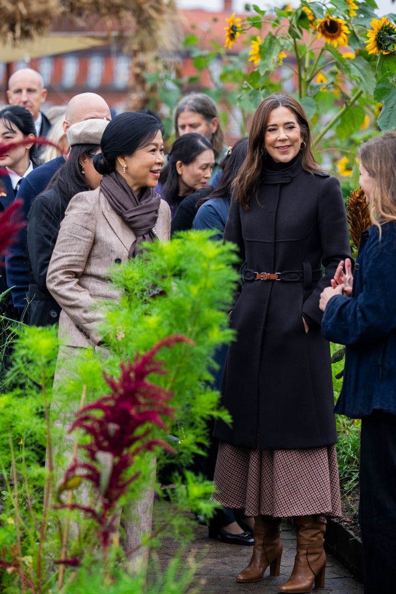 The Danish Queen embraced timeless fall fashion in a tailored navy Prada coat, patterned midi skirt and brown leather boots during a visit to a rooftop farm in Copenhagen.