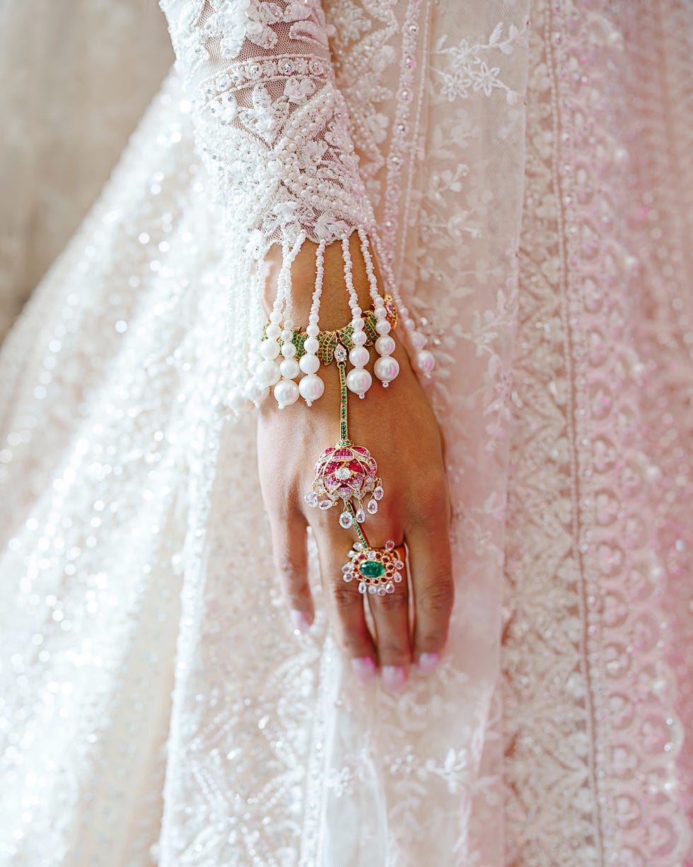 Close-up of a hand adorned with intricate jewelry and a beautifully embroidered dress.