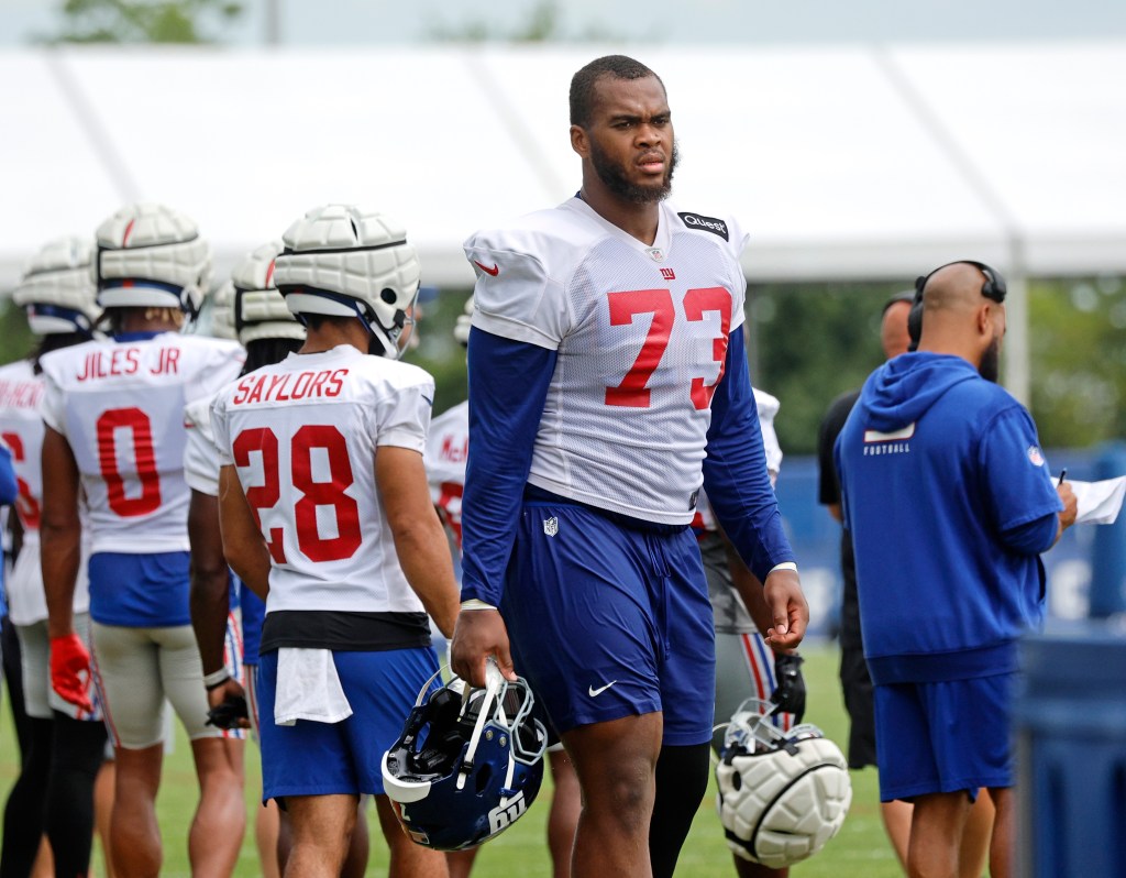 New York Giants offensive tackle Evan Neal stands on the sidelines holding his helmet during practice.