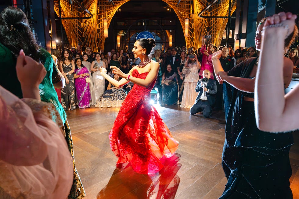 A vibrant celebration with a woman in a red dress dancing amid a crowd at a festive event.