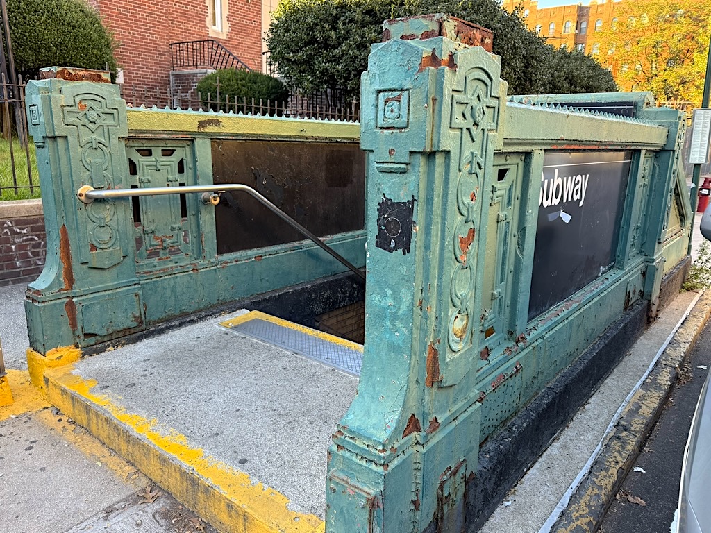 Vintage subway entrance with ornate turquoise metalwork, showing signs of rust and wear, leading down to the subway platform.